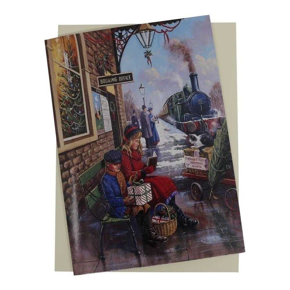 Steam Train Christmas card features a vintage steam train pulling into the station alongside a snow-covered platform with a young girl and boy sat with Christmas gifts outside the booking office.